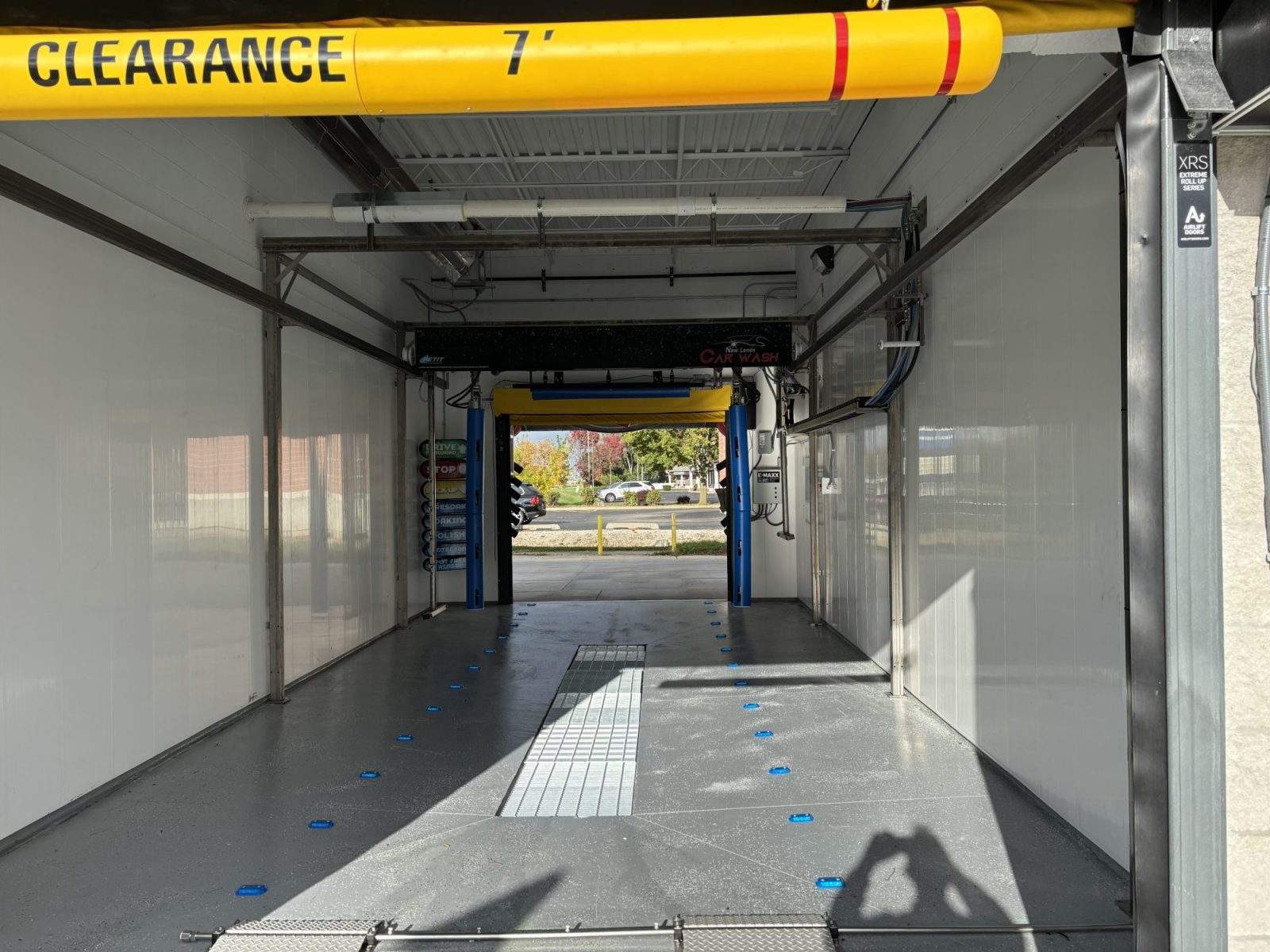 Remodel of New Lenox Car Wash with two Petit 360i units now open! Empty car wash bay with a 7-foot clearance sign overhead, white walls, a gray floor, and wash equipment visible on the sides and ceiling.