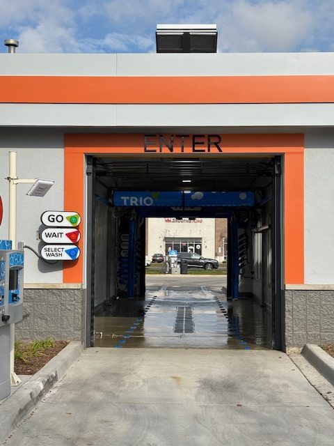 Drive-through car wash entrance with a sign labeled "ENTER" above, and a control panel displaying "GO," "WAIT," and "SELECT WASH" options on the left side.