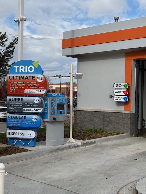 A car wash entrance with a price sign displaying wash options and an instruction signal with red, yellow, and green lights.