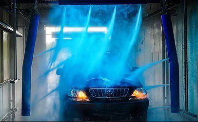 A black SUV is being sprayed with blue water jets inside an automated car wash bay.