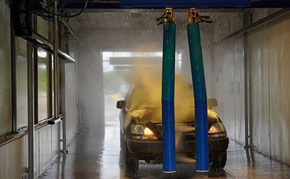 A black SUV is being sprayed with blue water jets inside an automated car wash bay.
