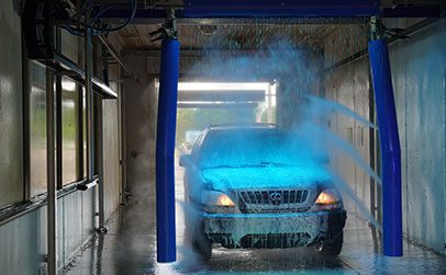A black SUV is being sprayed with blue water jets inside an automated car wash bay.