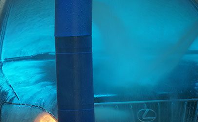 A black SUV is being sprayed with blue water jets inside an automated car wash bay.