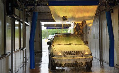 A black SUV is being sprayed with blue water jets inside an automated car wash bay.