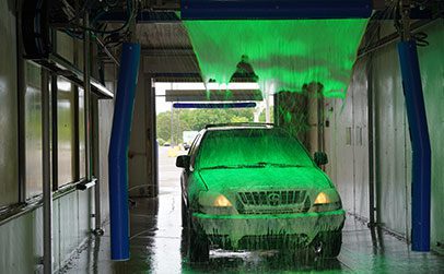 A black SUV is being sprayed with blue water jets inside an automated car wash bay.