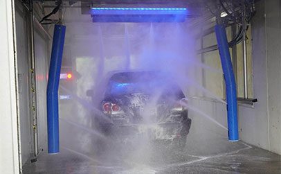 A black SUV is being sprayed with blue water jets inside an automated car wash bay.