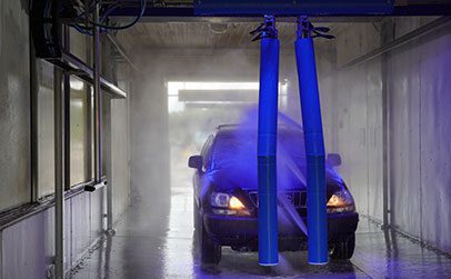 A black SUV is being sprayed with blue water jets inside an automated car wash bay.