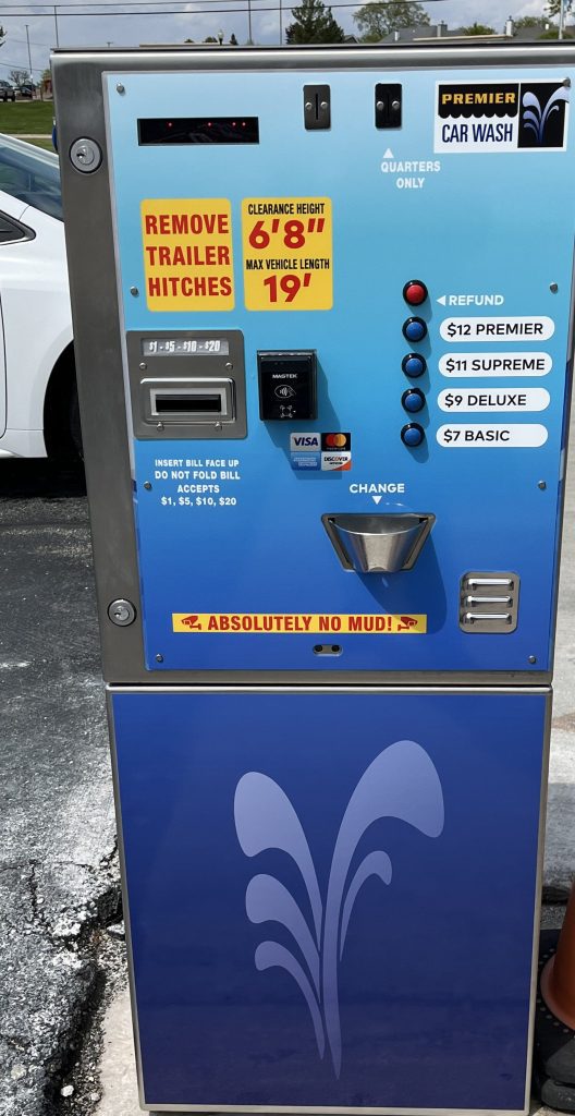 Blue self-service car wash payment kiosk with slots for cash, card, and coins, price options, refund button, and warning labels about height, length, and mud.