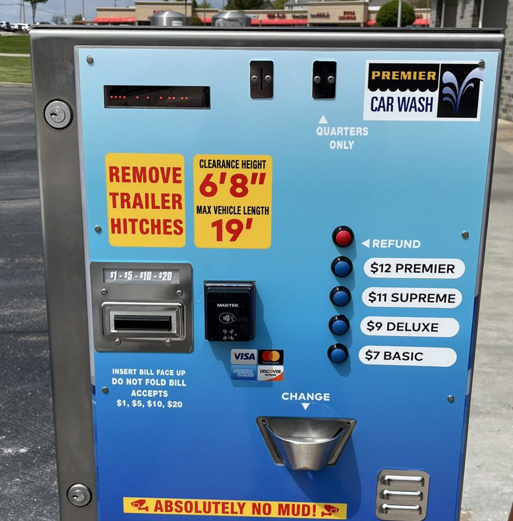 Blue self-service car wash payment machine with card slot, bill acceptor, coin slot, refund button, and package prices; warning labels visible.
