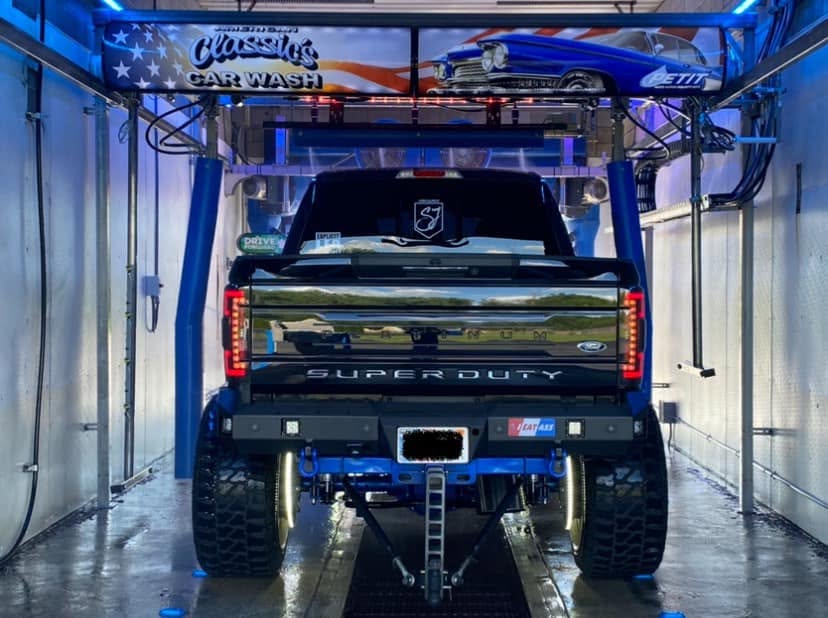 American Classic's Car Wash Finds Success with the Petit Accutrac®360-i A black Ford Super Duty truck with large tires is inside an automatic car wash bay with blue equipment and signage above.