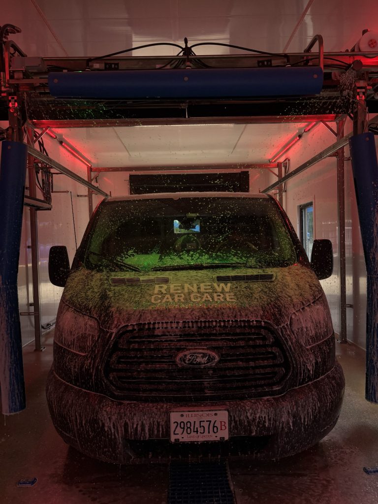 Two New Petit Accutrac® 360-i at Clean Machine Auto Wash A black Ford van covered in soap sits inside an automatic car wash with red lighting and "RENEW CARCARE" visible on the windshield.